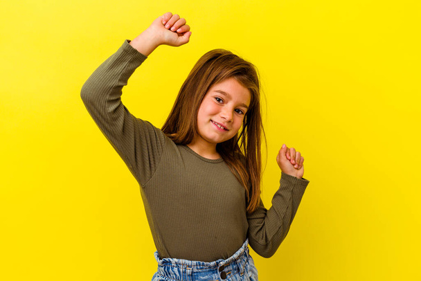 Kleines kaukasisches Mädchen, isoliert auf gelbem Hintergrund, feiert einen besonderen Tag, springt und hebt energisch die Arme. - Foto, Bild