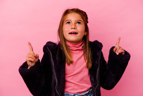 Little caucasian girl isolated on pink background  pointing upside with opened mouth. - Valokuva, kuva