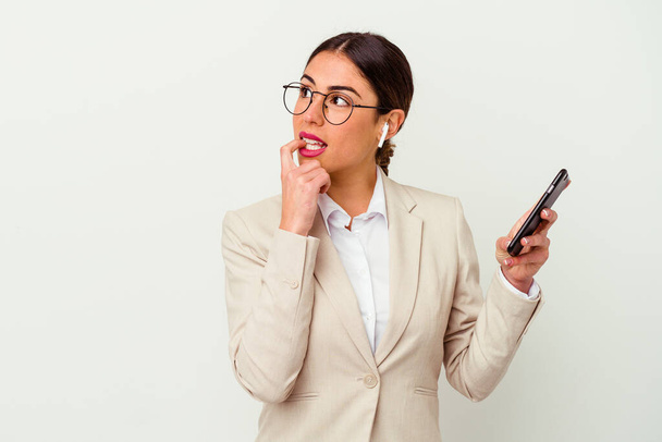 Mladá obchodní žena držící mobilní telefon izolované na bílém pozadí uvolněné myšlení o něco při pohledu na kopírovací prostor. - Fotografie, Obrázek