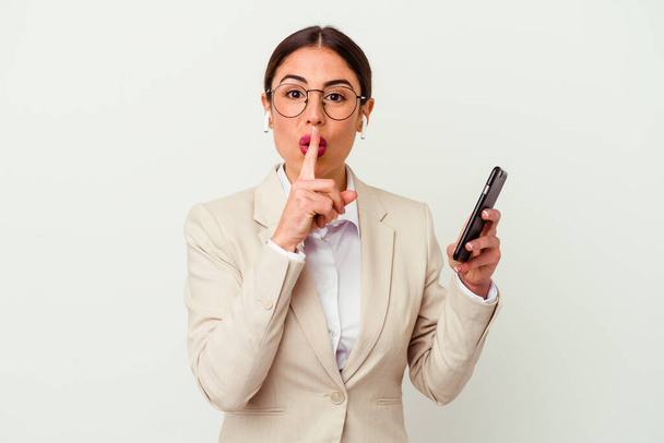 Joven mujer de negocios sosteniendo un teléfono móvil aislado sobre fondo blanco manteniendo un secreto o pidiendo silencio. - Foto, Imagen