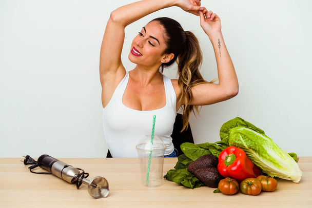 Mujer joven caucásica preparando un batido saludable con verduras brazos extendidos, posición relajada. - Foto, imagen