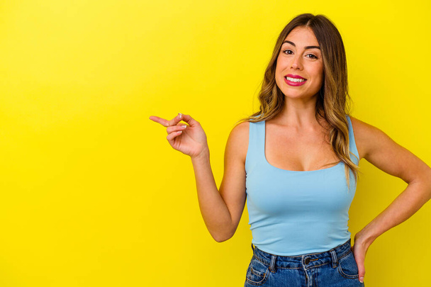 Junge kaukasische Frau isoliert auf gelbem Hintergrund lächelt fröhlich und zeigt mit dem Zeigefinger weg. - Foto, Bild