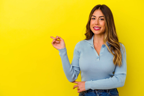Junge kaukasische Frau isoliert auf gelbem Hintergrund lächelt fröhlich und zeigt mit dem Zeigefinger weg. - Foto, Bild
