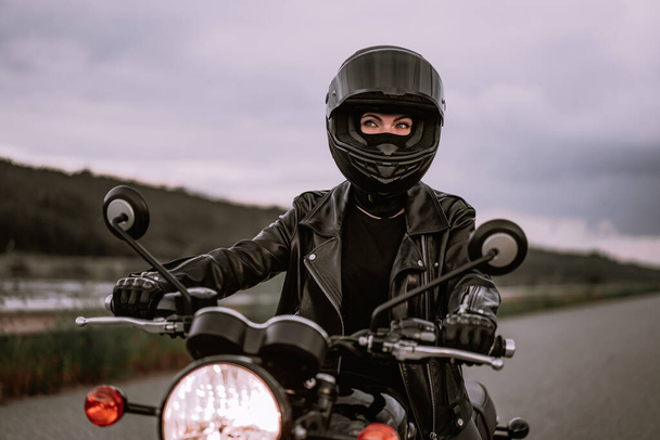 Portrait of confident motorcyclist woman in motorcycle helmet. Young driver biker looking away outdoors alone on highway. Ready for trip. Cafe racers, motorbike aesthetics and vintage design concept. - Photo, Image