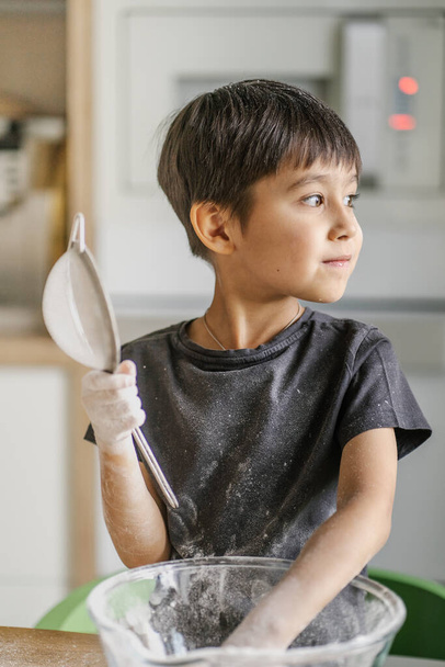 The child cooks in the kitchen. Sifts the flour. - Foto, Bild