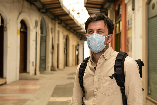 Gemaskerde mannelijke toeristische wandelingen op gesloten markt tijdens de coronavirus pandemie, lockdown op Cyprus. Man met masker loopt door de markt in het centrum van de stad. Geen toeristen, faillissement van kleine bedrijven onder COVID 19. - Foto, afbeelding