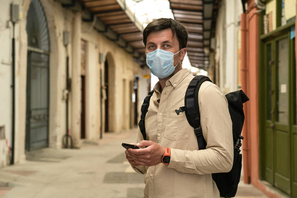 Des touristes masculins masqués marchent au marché fermé pendant la pandémie de coronavirus, enfermés à Chypre. Homme masqué marche à travers le marché dans le centre-ville. Pas de touristes, faillite de petites entreprises sous COVID 19. - Photo, image
