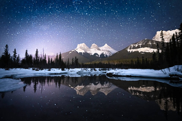 Alpejska scena nocna z niebem pełnym gwiazd i gór odbitych w powierzchni wody, nakręcona w Canmore, Alberta, Kanada - Zdjęcie, obraz