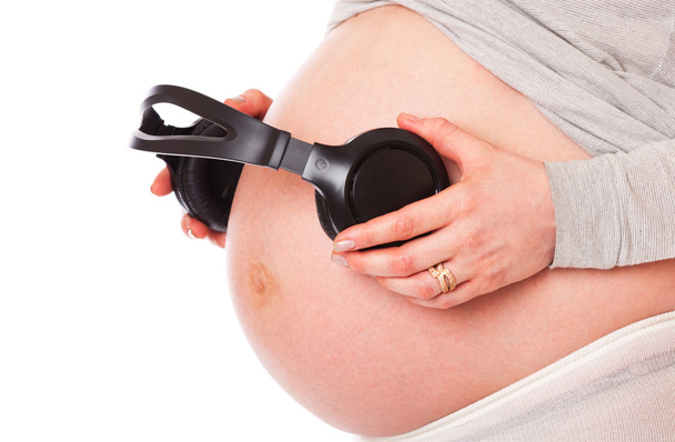 A belly of pregnant woman with headphones. isolated on a white background - Foto, Imagen