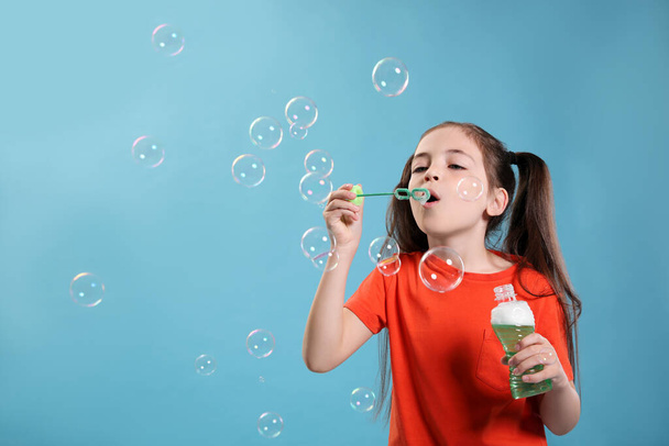 Little girl blowing soap bubbles on light blue background, space for text - Фото, зображення