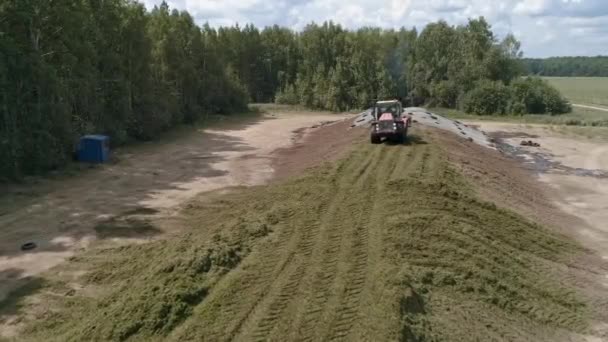 Drone view of tractor tamp the silage in the Silo Trench next to the forest and field. Forage For Animals. Summer sunny day - Felvétel, videó