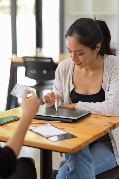 Designer freelance feminino projetando sua coleção via tablet inteligente com caneta caneta stylus no café durante sair com o amigo - Foto, Imagem