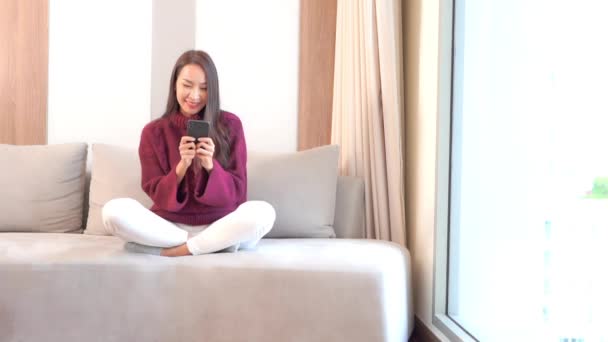 πλάνα από όμορφη νεαρή ασιατική γυναίκα χρησιμοποιώντας smartphone στο σπίτι - Πλάνα, βίντεο