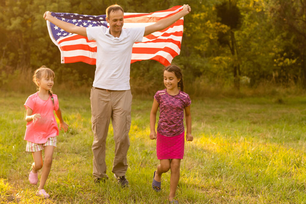 Família feliz no campo com os EUA, bandeira americana nas costas. - Foto, Imagem