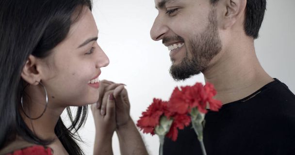 A closeup shot of a young Indian couple holding red flowers - Фото, изображение
