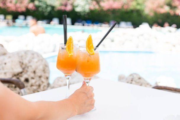Zumo de naranja en vaso de cóctel en mesa de madera en la piscina al aire libre, concepto de vacaciones tropicales de verano - Foto, imagen
