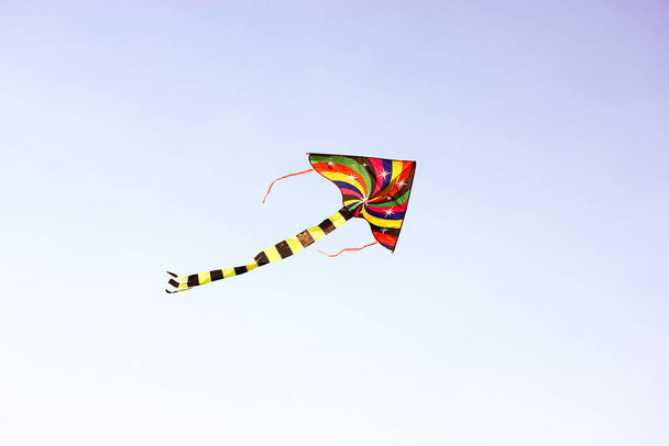 Ярко разноцветный воздушный змей летит на ветру высоко в небе. Детские развлечения, развлечения на свежем воздухе для детей летом. Концепция свободы, радости, летних каникул, отдыха в детском лагере - Фото, изображение