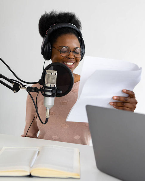 African American woman with headphones and a microphone recording a podcast in a recording studio - Фото, зображення