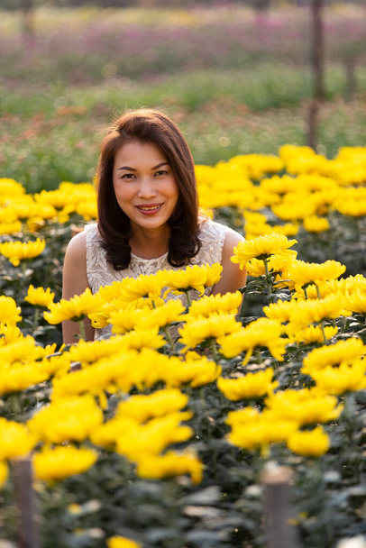 Gyönyörű ázsiai nő áll és mosolyog a trópusi virágos kertben boldogság módon meleg napfény a háttérből. - Fotó, kép