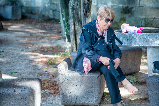 Mujer anciana cansada relajando sus pies en un banco público de la ciudad - Foto, imagen