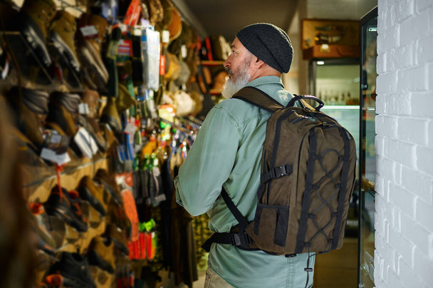 Hunter with backpack at the showcase in gun store - Photo, Image
