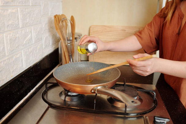 Vrouw gieten plantaardige olie in koekenpan bij het koken van ontbijt of diner in de keuken - Foto, afbeelding