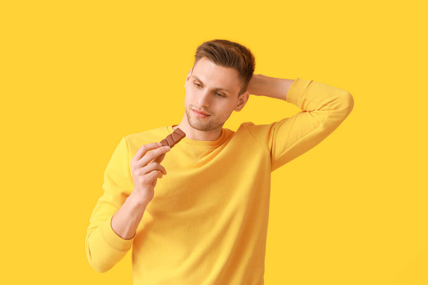 Bello giovane uomo con gustoso cioccolato su sfondo di colore - Foto, immagini