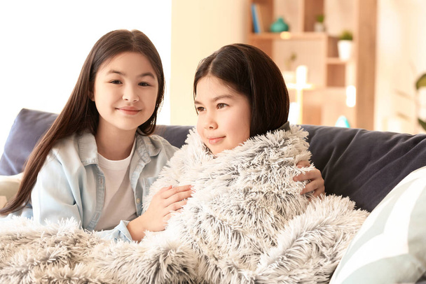 Cute Asian sisters with plaid resting on sofa at home - Foto, immagini