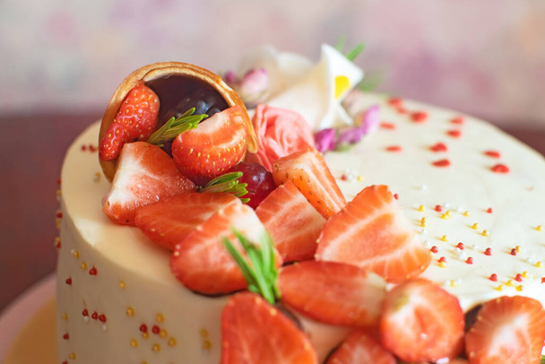 Close-up of beautiful birthday cake with strawberries, marmalades, waffle cone and mastic flowers decor on the table. - Foto, imagen