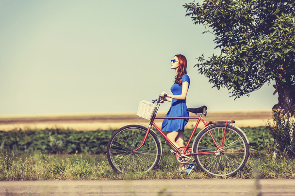 Ragazza rossa con bicicletta sulla strada di campagna
. - Foto, immagini