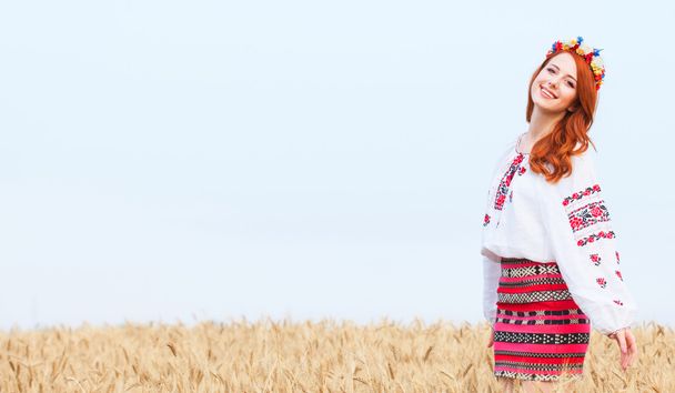 Redhead girl in national ukrainian clothes on the wheat field. - Photo, Image