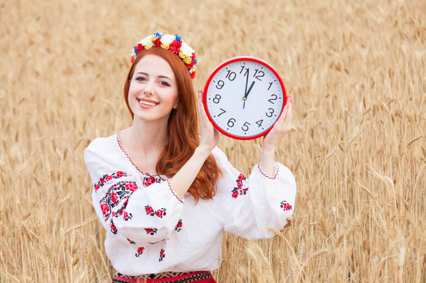 roodharige meisje in nationale Oekraïense kleren met klok op de whe - Foto, afbeelding
