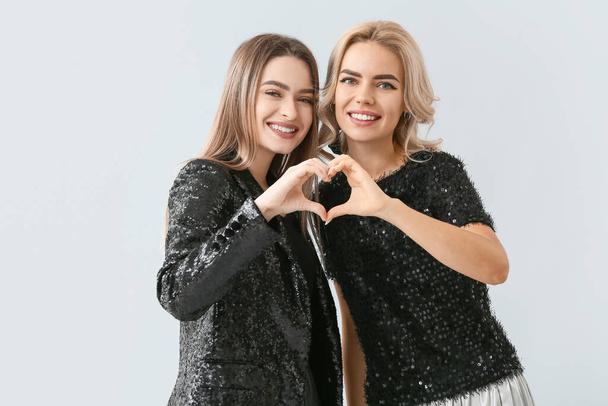 Όμορφες νεαρές αδελφές κάνουν σχήμα καρδιάς με τα χέρια τους στο φως φόντο - Φωτογραφία, εικόνα