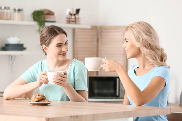 Beautiful young sisters drinking tea in kitchen - Фото, изображение