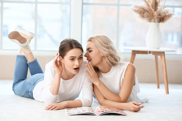 Young woman telling her sister secret at home - Foto, imagen