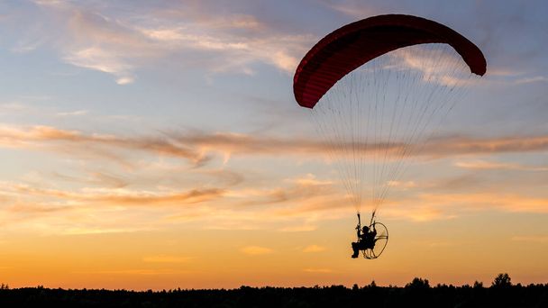 Silueta piloto de parapente accionado con motor montado en la parte posterior (paramotor) durante la puesta del sol - Foto, imagen