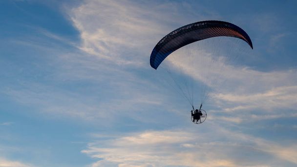 Silhouet van aangedreven paraglider tegen de blauwe lucht - Foto, afbeelding