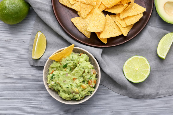 Bowl with tasty guacamole and nachos on color wooden background - Photo, Image