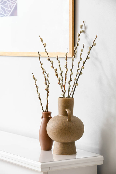 Vases with willow branches on shelf near light wall - Foto, imagen