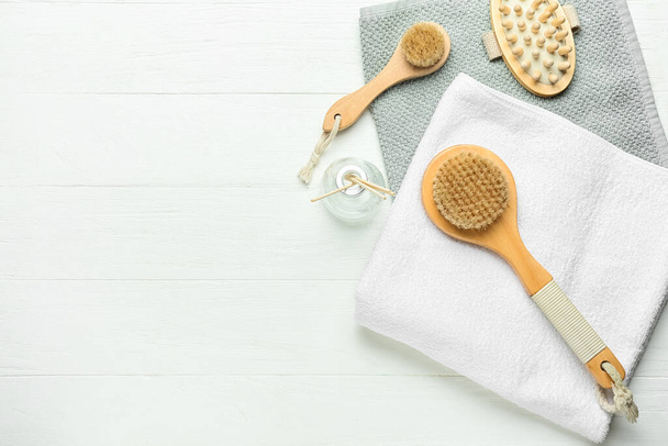 Different massage brushes and towels on light wooden background - 写真・画像
