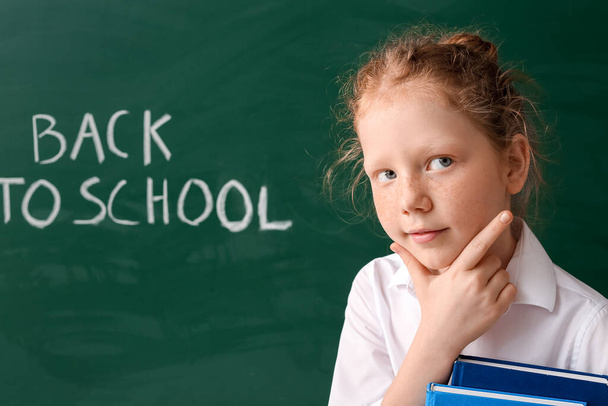 Χαριτωμένο κοριτσάκι κοντά μαυροπίνακα στην τάξη - Φωτογραφία, εικόνα
