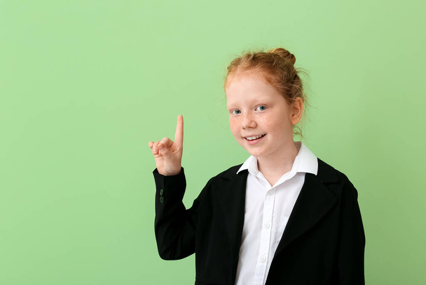 Cute little schoolgirl with raised index finger on color background - Foto, Imagem