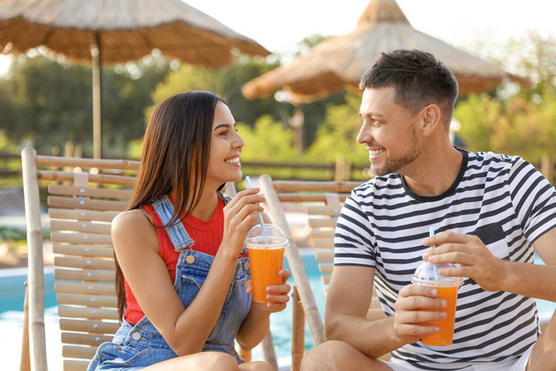 Happy couple with cups of refreshing drink resting in deck chairs  - Foto, Imagen