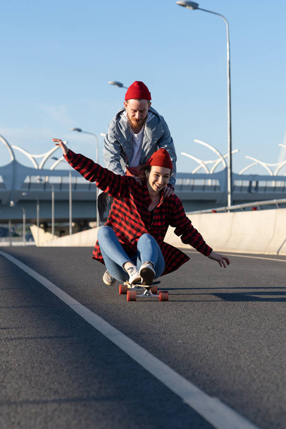 Happy lovers couple chill outdoors ride longboard, laugh and have fun together on urban city road - Foto, Imagem