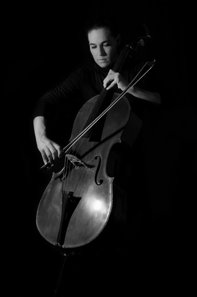 Beautiful brunette playing a cello with selective light in black - Photo, image