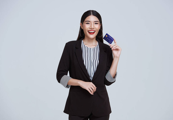Smiling Confident Asian business woman showing credit card isolated on gray background.	 - Foto, Bild