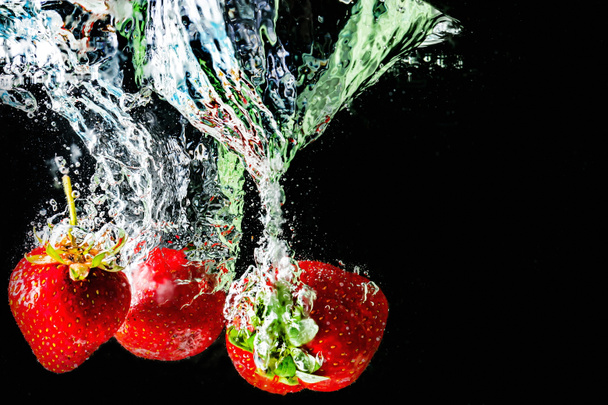 reife Erdbeeren fallen ins Wasser und heben Spritzer und Luftblasen - Foto, Bild