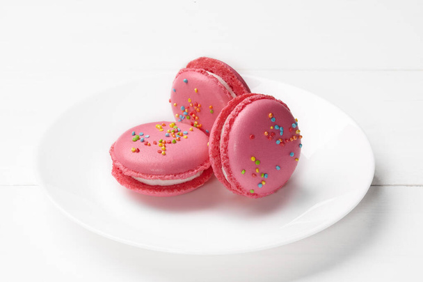 Három rózsaszín makaróni krémes töltelékkel és cukorral a tányéron. - Fotó, kép