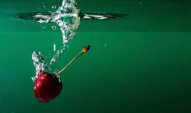 ripe cherries fall into the water raising splashes and air bubbles - Photo, Image