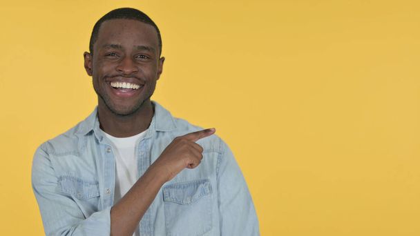 Hombre joven africano señalando el producto, fondo amarillo  - Foto, Imagen